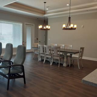 A modern dining room with a large table, multiple chairs, and chandeliers hanging from the ceiling.