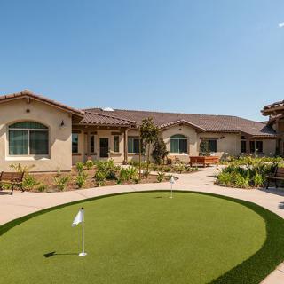 A sunny view of a building with a small putting green in the foreground.