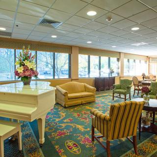A spacious lounge area with a white piano, comfortable seating, and large windows providing natural light.