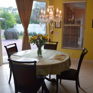 A cozy dining room with a round table set for four, adorned with sunflowers, and a chandelier overhead.