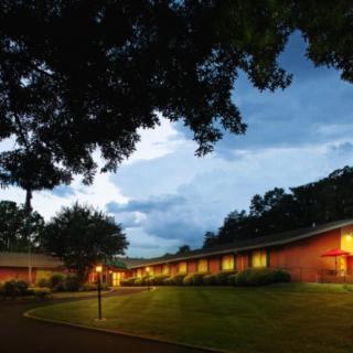A tranquil evening scene featuring a building softly illuminated by lights, surrounded by trees and an expansive sky.