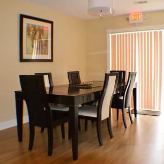 A modern dining room with a dark wood table and six matching chairs on a wooden floor, complemented by artwork on the wall.
