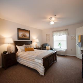 A well-decorated bedroom featuring a bed with striped bedding, two bedside tables with lamps, and a window providing natural light.