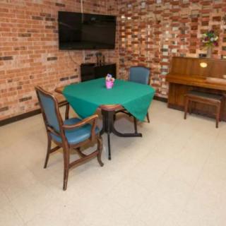 A cozy living room with a table and chairs, brick walls, a television, and a piano.