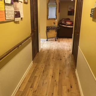 A cozy hallway with wooden flooring, yellow walls, and a mirror leading to a furnished room.