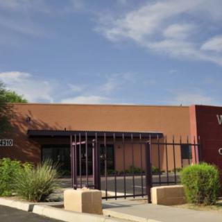 A small, gated building under a partly cloudy sky with desert vegetation.