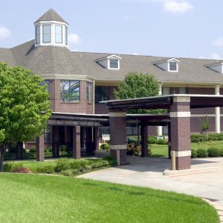 A modern building with a prominent entrance and surrounding greenery under a clear sky.
