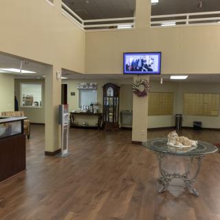 A modern lobby with a reception area, featuring a wooden floor, glass tables, and a wall-mounted television.