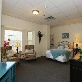 A cozy bedroom with stylish decor, featuring a bed, two chairs by the window, and ambient lighting.