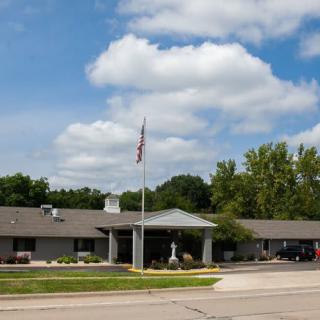 A one-story building with an American flag flying in front, surrounded by trees and under a partly cloudy sky.