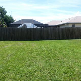 A neatly mowed backyard with a wooden fence and houses in the background.