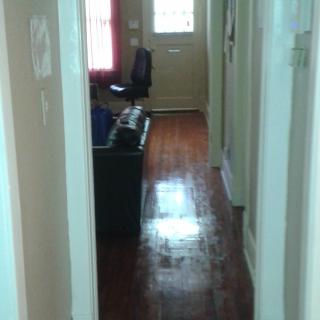 A view down a hallway with wooden floors leading to a door and furnished room.