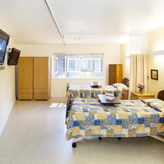 A clean hospital room with two beds, a television, and a wardrobe.