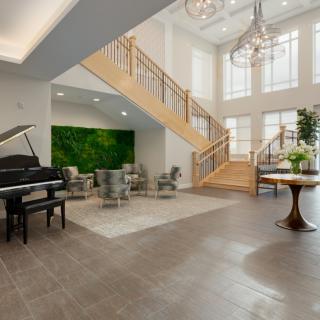 A spacious and modern lobby featuring a grand piano, elegant staircase, and stylish furnishings.