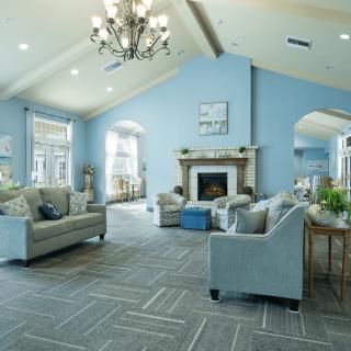 A spacious and elegantly designed living room with blue walls, featuring a chandelier, cozy furniture, and a fireplace.