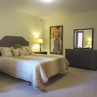A cozy bedroom featuring a bed with decorative pillows, two bedside lamps, a dresser with a mirror, and artwork on the wall.