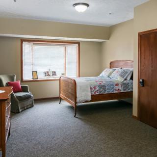 A cozy bedroom with a bed, armchair, and large window.