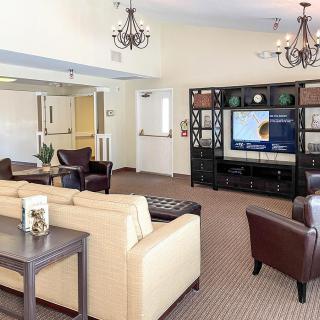 A spacious and elegantly decorated living room featuring comfortable seating, a large television, and stylish chandeliers.