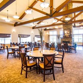 A spacious dining hall with wooden beams, warm lighting, and neatly arranged tables and chairs.