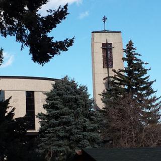 A church building featuring a prominent tower and surrounded by trees under a blue sky.