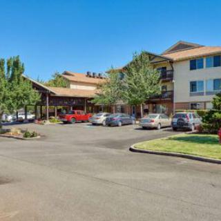 A hotel with a parking lot in front, surrounded by trees under a clear blue sky.