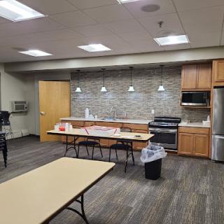 A modern breakroom featuring a kitchen area with wooden cabinets, appliances, and seating arrangements.