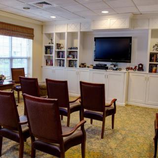 A cozy meeting room with arranged chairs facing a television and bookshelves.
