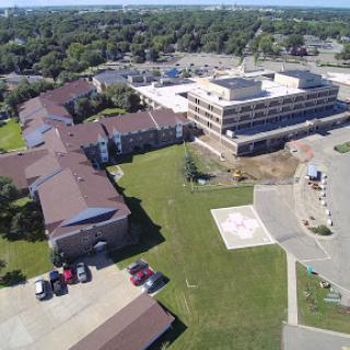 An aerial view of a construction site alongside existing buildings, highlighting green spaces and parking areas.