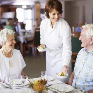 A waitress serves food to an elderly couple at a restaurant.