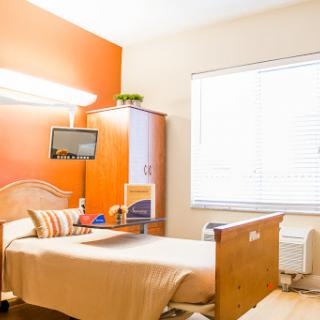 A cozy hospital room featuring a bed, modern furnishings, and natural light from a large window.