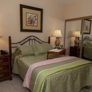 A cozy bedroom with a neatly made bed, nightstands, lamps, and mirrored closet doors.