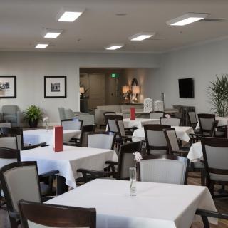 A modern, empty dining room with neatly arranged tables and chairs, adorned with white tablecloths.