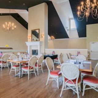 An elegant restaurant dining area featuring chandeliers, a fireplace, and neatly arranged tables and chairs.
