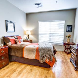 Cozy and well-decorated bedroom with a wooden floor, featuring a bed, nightstands with lamps, and a large window letting in natural light.