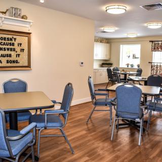 A cozy dining area with blue chairs, tables, and a small kitchen in the background.