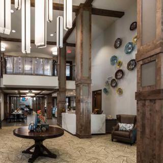A spacious and modern lobby featuring decorative plates on the wall, wooden columns, and a central table beneath a chandelier.