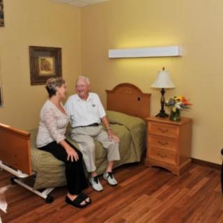 An elderly couple sitting on a bed in a cozy nursing home room.
