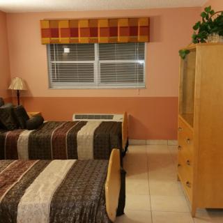 A cozy bedroom with twin beds featuring striped bedding, a window with curtains, and a dresser topped with a plant.