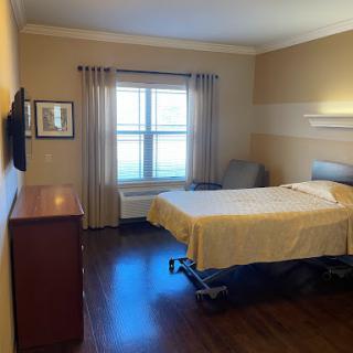 A well-lit hospital room featuring a bed, TV, and large window with curtains.