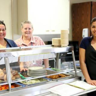 Cafeteria staff members standing behind a lunch counter ready to serve.