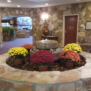 A cozy lobby with a central fountain surrounded by colorful flowers and stone walls.