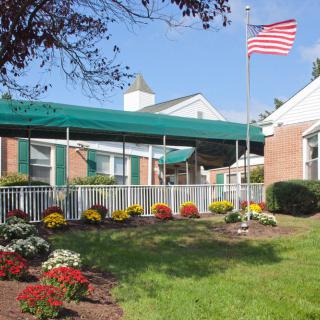 A building with a green awning and landscaped garden featuring colorful flowers and an American flag.