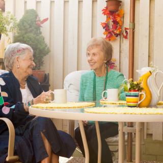 Two elderly women enjoying a conversation over tea on a sunny patio.