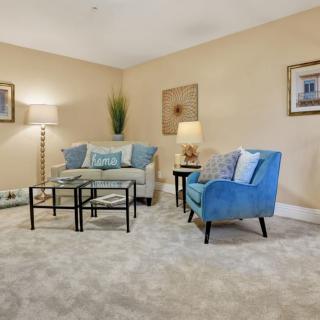 A cozy living room with beige walls featuring a sofa, blue armchair, and coffee table, complemented by decorative artwork and lamps.