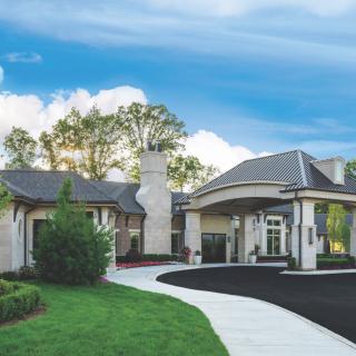 A modern house with a landscaped garden and driveway under a blue sky.