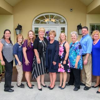 A group of people standing together in formal attire outside a building, smiling for a photo.