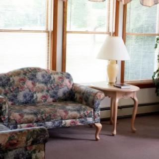 A cozy living room with a floral upholstered couch, side table, and lamp, bathed in natural light from spacious windows.