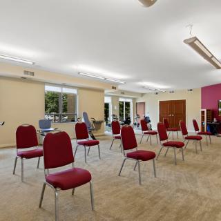 A spacious meeting room with red chairs arranged in a socially distanced setup.