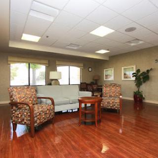 A cozy waiting area featuring comfortable chairs, a small table, and natural light from large windows.