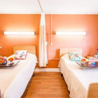 A bright and modern bedroom with twin beds against an orange wall, featuring colorful pillows and sleek lighting.